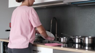 Side view of woman cleaning a ceramic plate under water stream, holding it with pink gloves