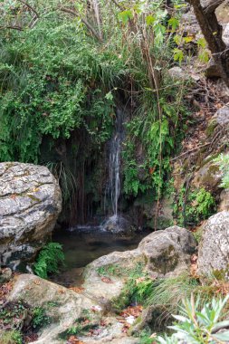 Polylimnio waterfall cascade in Peloponnese, Greece, surrounded by moss-covered rocks and lush Mediterranean vegetation