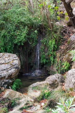 Polylimnio waterfall cascade in Peloponnese, Greece, surrounded by moss-covered rocks and lush Mediterranean vegetation