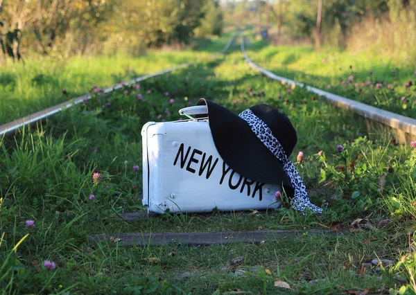 suitcase old  with  inscription NEW YORK  and a hat   on railway tracks