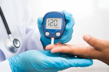 Diyabet tedavisinde kan şekeri seviyesini kontrol etmek için dijital glikoz ölçer kullanan Asyalı doktor.