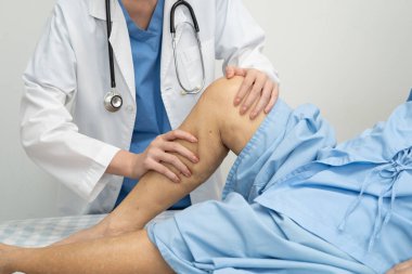 Doktor, hastanede dizinde yara izi olan Asyalı yaşlı kadın hastayı kontrol ediyor..