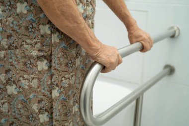 Asyalı yaşlı kadın hasta tuvaletteki destek parmaklıklarında tırabzan emniyeti kullanıyor..