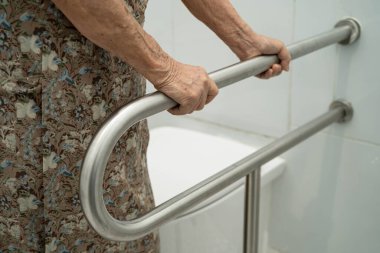 Asyalı yaşlı kadın hasta tuvaletteki destek parmaklıklarında tırabzan emniyeti kullanıyor..