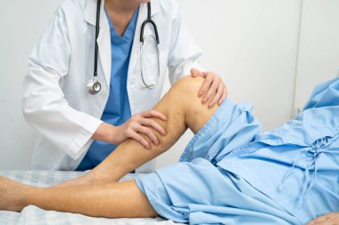 Doktor, hastanede dizinde yara izi olan Asyalı yaşlı kadın hastayı kontrol ediyor..