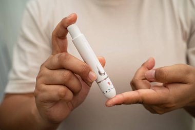 Evde parmak üzerinde dijital mızrakla kan şekeri seviyesini ölçmek için Asyalı kadın kendini test ediyor..