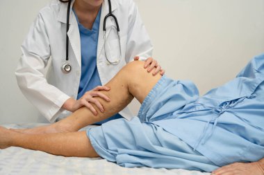 Doktor, hastanede dizinde yara izi olan Asyalı yaşlı kadın hastayı kontrol ediyor..