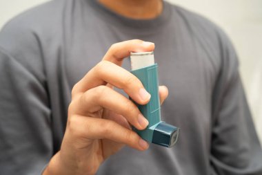 Astım ve kronik obstrüktif akciğer hastalığı COPD, Asyalı genç adam ölçülü doz solunum cihazı kullanıyor..