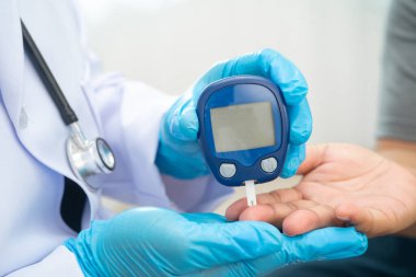 Diyabet tedavisinde kan şekeri seviyesini kontrol etmek için dijital glikoz ölçer kullanan Asyalı doktor.