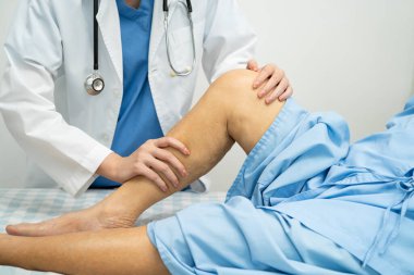 Doktor, hastanede dizinde yara izi olan Asyalı yaşlı kadın hastayı kontrol ediyor..