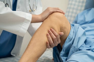 Doktor, hastanede dizinde yara izi olan Asyalı yaşlı kadın hastayı kontrol ediyor..