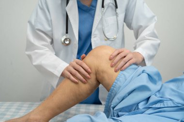 Doktor, hastanede dizinde yara izi olan Asyalı yaşlı kadın hastayı kontrol ediyor..