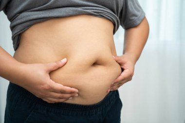 Asyalı kadın şişman göbeğini sıkmak için elini kullanıyor. Büyük boy aşırı kilolu ve obez..