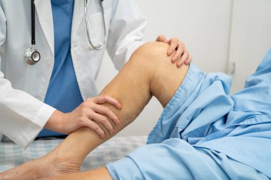 Doktor, hastanede dizinde yara izi olan Asyalı yaşlı kadın hastayı kontrol ediyor..