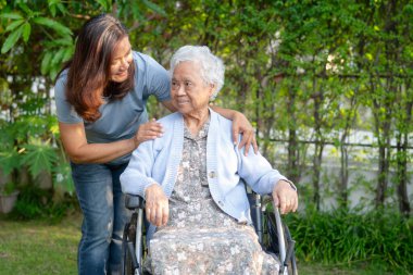Bakıcı, parkta tekerlekli sandalyede oturan Asyalı yaşlı kadın engelli hastaya yardım ediyor..