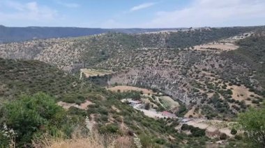 Dağınık ağaçlar, kayalık yamaçlar, toprak yollar ve kırmızı çatıları olan küçük çiftlik binalarıyla dolu dik bir Kıbrıs Vadisi 'ndeki uzak bir kırsal arazinin klibi, Akdeniz kırsal kesimini gösteriyor.