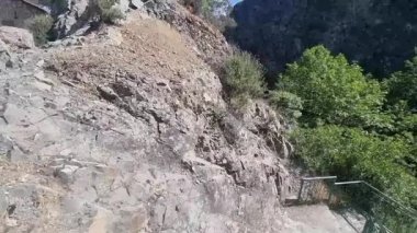 Kıbrıs 'ın Troodos Dağları' ndaki çam ağaçları ve mavi gökyüzünün ortasında dik kayalıklara tünemiş taştan bir ev videosu geleneksel dağ köyü mimarisi ile uyumlu.