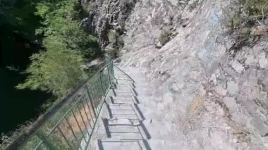 Dik beton adımların videosu, yeşil metal korkulukların kayalık bir uçurum duvarını sararak Kıbrıs dağlarında seyrek çalılarla çevrili, şelalelere ve manzaraya heyecan verici bir erişim sağlıyor.