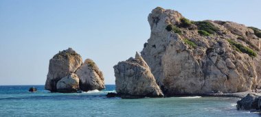 Yeşil bitki örtüsü ve yosun parçalarıyla kaplı, denizden çarpıcı biçimde yükselen büyük, engebeli kireç taşı oluşumlarının çarpıcı yakın çekimi. Açık gri ve bej kayalar desenli