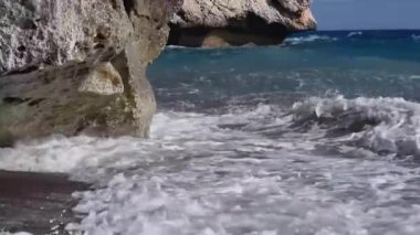 Kıbrıs 'taki Afrodit Sahili' nde büyük bir kıyı kayası ve kumlu sahile vuran Akdeniz dalgalarının yakın çekimi romantik, mitolojik, rahatlatıcı ve yaz tatili kavramları için mükemmeldir..