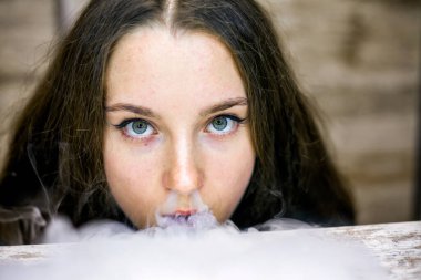 Buharlı genç. İçeride elektronik sigara içen uzun saçlı beyaz, beyaz, genç bir kız. Çok kötü bir alışkanlık. Vestiyer etkinliği.