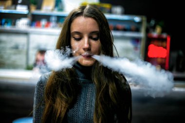 Buharlı genç. İçeride elektronik sigara içen uzun saçlı beyaz, beyaz, genç bir kız. Çok kötü bir alışkanlık. Vestiyer etkinliği.