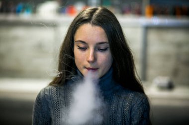 Buharlı genç. İçeride elektronik sigara içen uzun saçlı beyaz, beyaz, genç bir kız. Çok kötü bir alışkanlık. Vestiyer etkinliği.