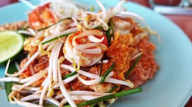 Mavi bir tabakta servis edilen karides, pirinç eriştesi, fasulye filizi, tofu ve fıstıklı Pad Thai 'nin yakın çekimi..