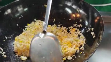 Chef stir-frying egg fried rice in a hot black wok with a metal spatula.