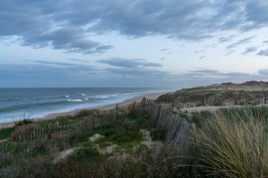 Fransa 'da fırtınalı bir gökyüzünün altında sonsuz bir plajda kum tepeleri ve dalgalar kırılıyor.