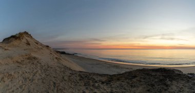 Güneş doğarken kumulları olan vahşi bir sahil ve okyanus.
