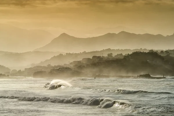 A mountain landscape in silhouette with beach and waves breaking in the foreground