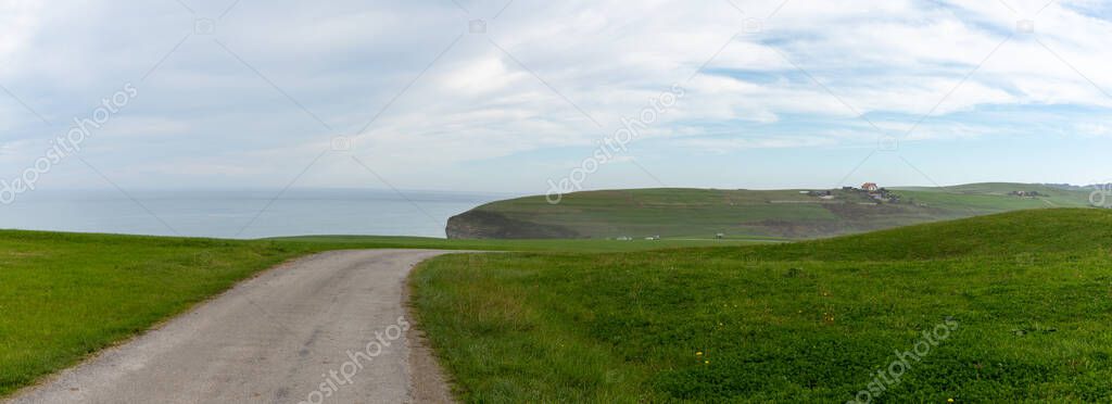 panorama of country roaad leading to ocean and steep cliffs in green coastal landscape