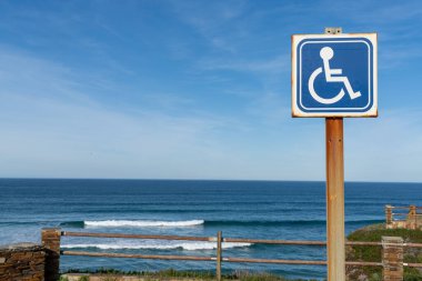 Arkasında okyanus olan bir sahil girişinde engelli park yeri tabelası.