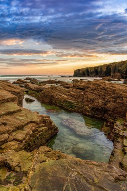 Beautiful sunrise at the Playa de las Catedrales Beach in Galicia in northern Spain with tidal pools in the foreground clipart