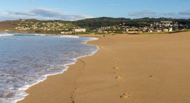 Kumsalda bir sürü ayak izi ve uzaklarda yürüyen bir kadın.