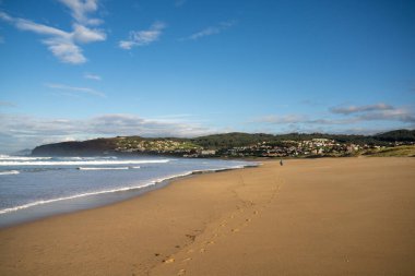 Kumsalda bir sürü ayak izi ve uzaklarda yürüyen bir kadın.