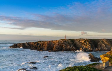 Gün batımında engebeli Alentejo kıyı şeridi ve Porto Covo deniz feneri manzarası