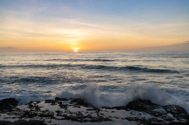 Gün batımında gel-git havuzlarıyla kayalık sahile vuran büyük dalgaların görüntüsü