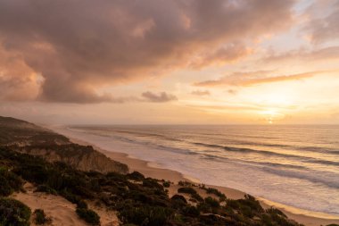 Portekiz 'in Alentejo sahilinde kumulları olan güzel bir günbatımı.