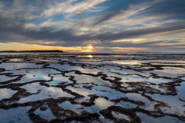 Okyanusun üzerinde güzel bir gün batımı kayalık plajlar ve ön planda gelgit havuzları.