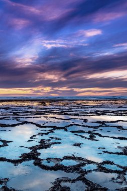 Okyanusun üzerinde kayalık plajlı ve ön planda gelgit havuzlu güzel bir gün batımının dikey görüntüsü.