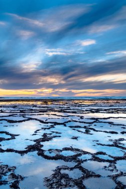 Okyanusun üzerinde kayalık plajlı ve ön planda gelgit havuzlu güzel bir gün batımının dikey görüntüsü.