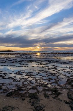 Okyanusun üzerinde kayalık plajlı ve ön planda gelgit havuzlu güzel bir gün batımının dikey görüntüsü.