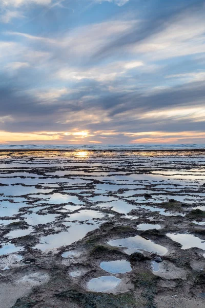 Okyanusun üzerinde kayalık plajlı ve ön planda gelgit havuzlu güzel bir gün batımının dikey görüntüsü.