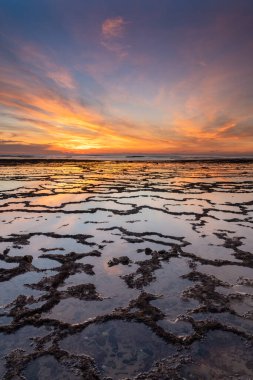 Okyanusun üzerinde kayalık plajlı ve ön planda gelgit havuzlu güzel bir gün batımının dikey görüntüsü.