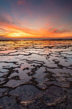 Okyanusun üzerinde kayalık plajlı ve ön planda gelgit havuzlu güzel bir gün batımının dikey görüntüsü.