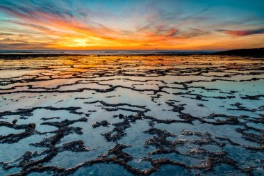 Okyanusun üzerinde güzel bir gün batımı kayalık plajlar ve ön planda gelgit havuzları.