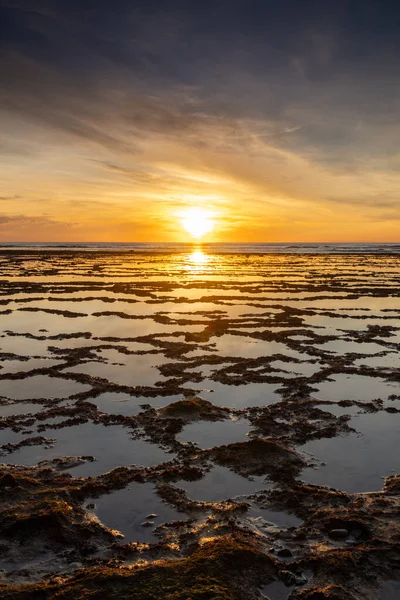 Okyanusun üzerinde kayalık plajlı ve ön planda gelgit havuzlu güzel bir gün batımının dikey görüntüsü.