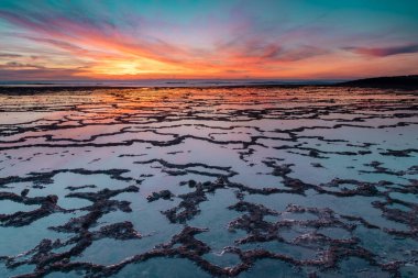Okyanusun üzerinde güzel bir gün batımı kayalık plajlar ve ön planda gelgit havuzları.